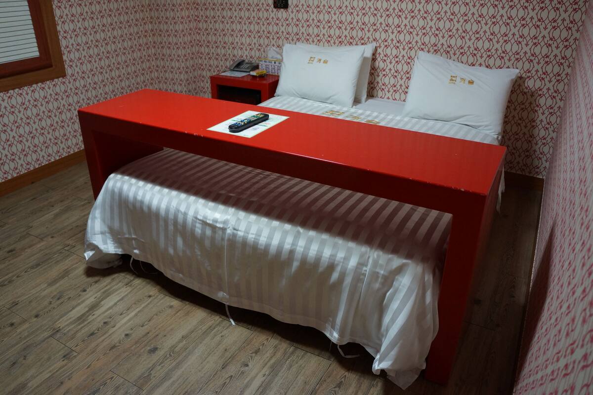 A room with a bed, a red table, and a wooden floor.
