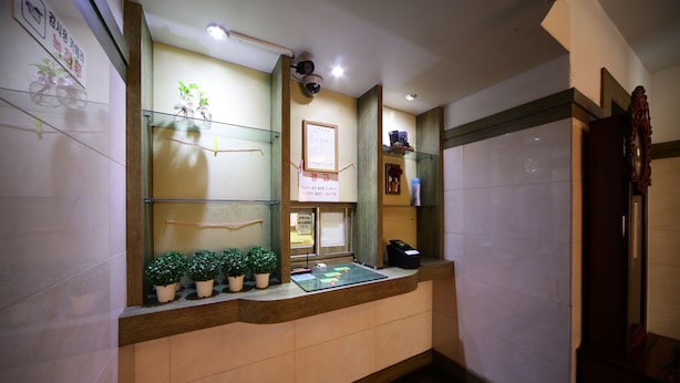 A reception desk with potted plants, a framed notice, and a security camera. - Castle Motel Iksan (Iksan)
