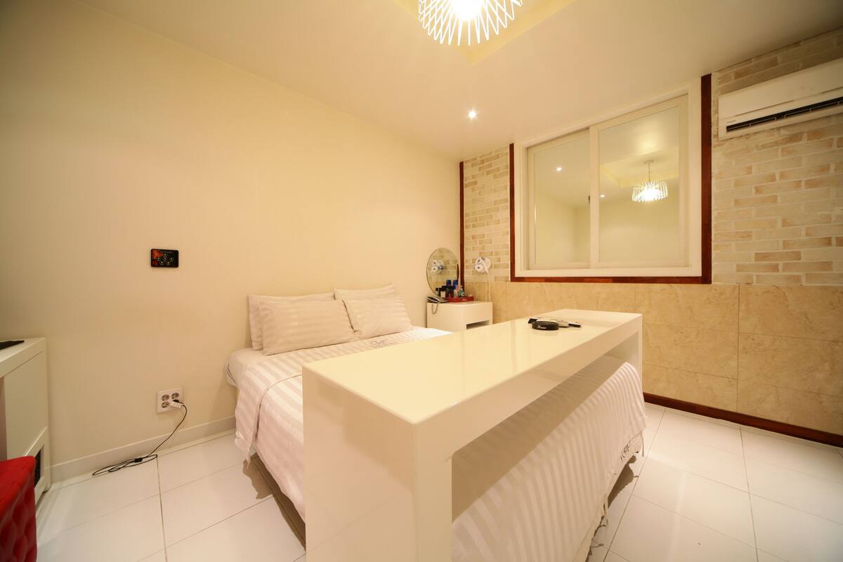 A modern bedroom with a large bed, a bedside table, a mirror, and a built-in vanity with a mirror.