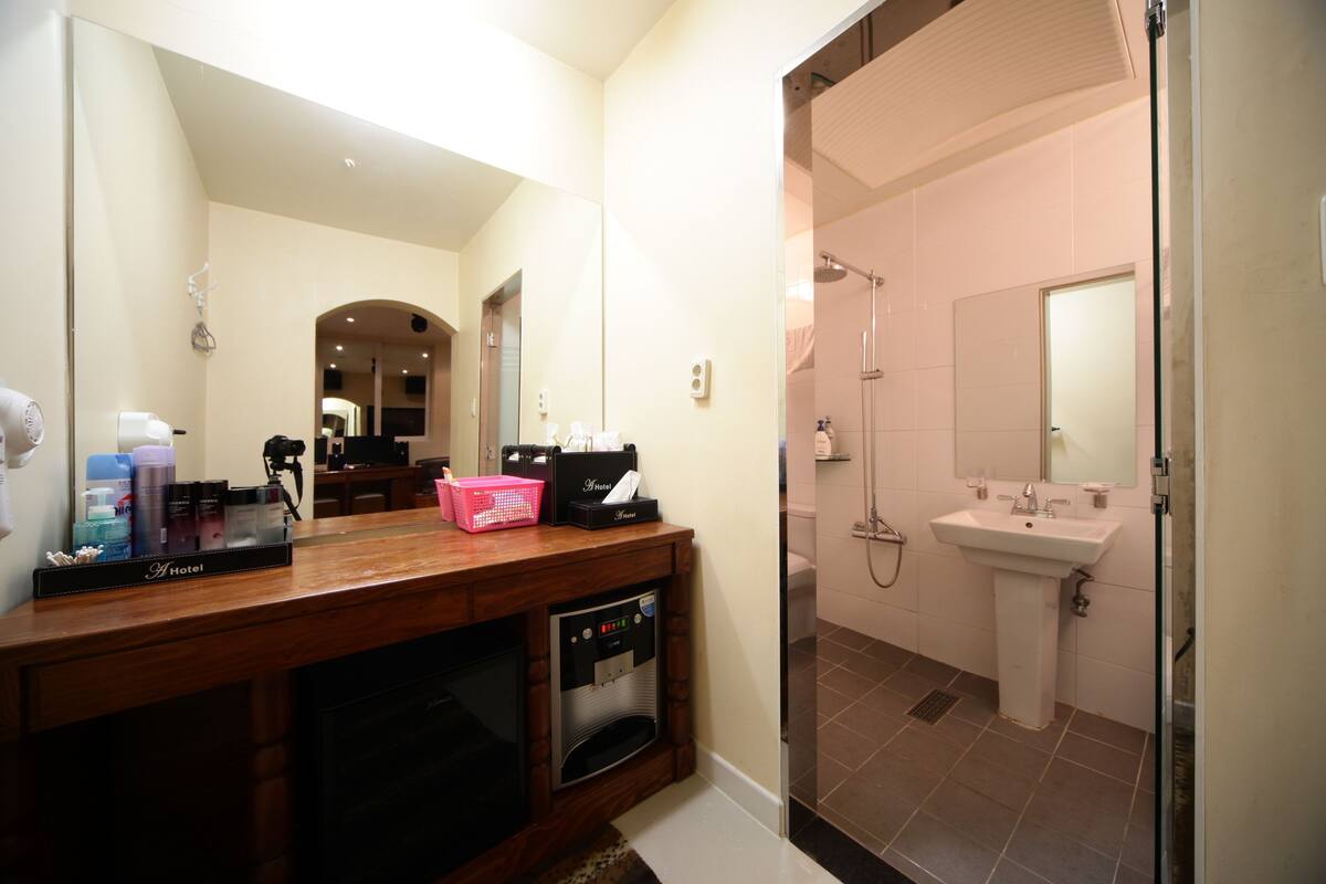 A hotel bathroom with a wooden vanity, a sink, a mirror, and a shower.