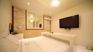 Una habitación de hotel con cama, televisión montada en la pared, espejo y ventana.