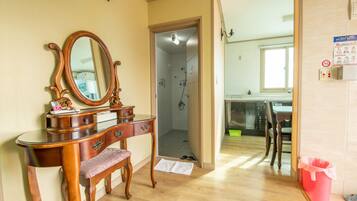 Quarto com toucador de madeira, espelho, banco e área de chuveiro.