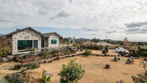 A residential property with a brick house, a small garden, and a car parked nearby. - Lionhill Pension (Seogwipo)