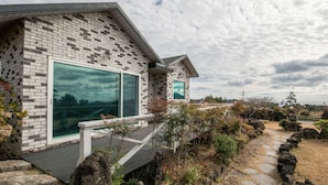 A modern house with a brick exterior, large windows, and a stone pathway leading to the entrance. - Lionhill Pension (Seogwipo)