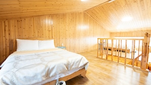 A wooden-paneled bedroom with a bed, a nightstand, and a wooden staircase. - Lionhill Pension (Seogwipo)