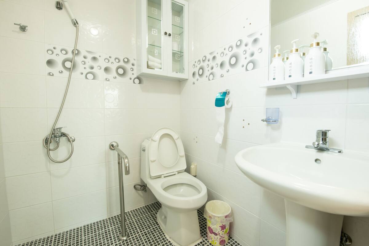 A bathroom with a toilet, shower, sink, and a cabinet with toiletries.