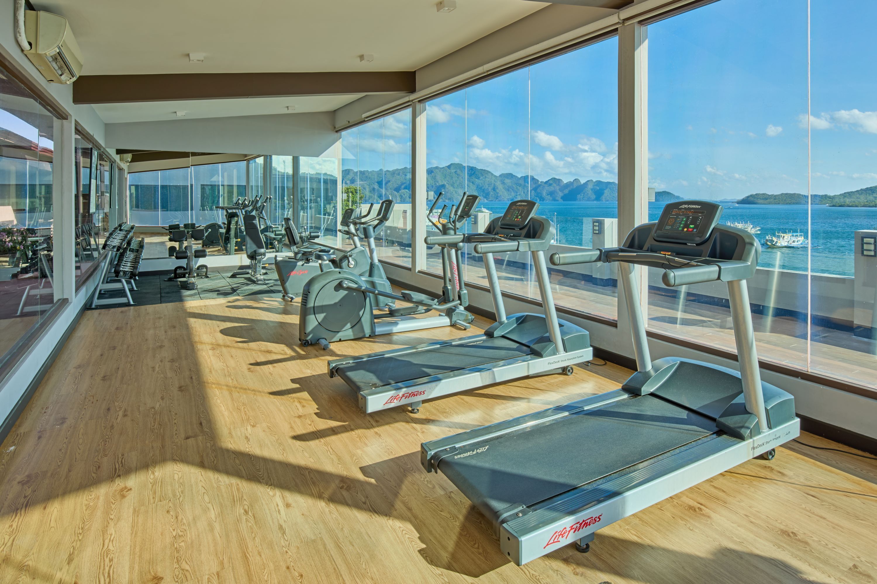 A gym with treadmills and exercise equipment, large windows, and a view of the sea.