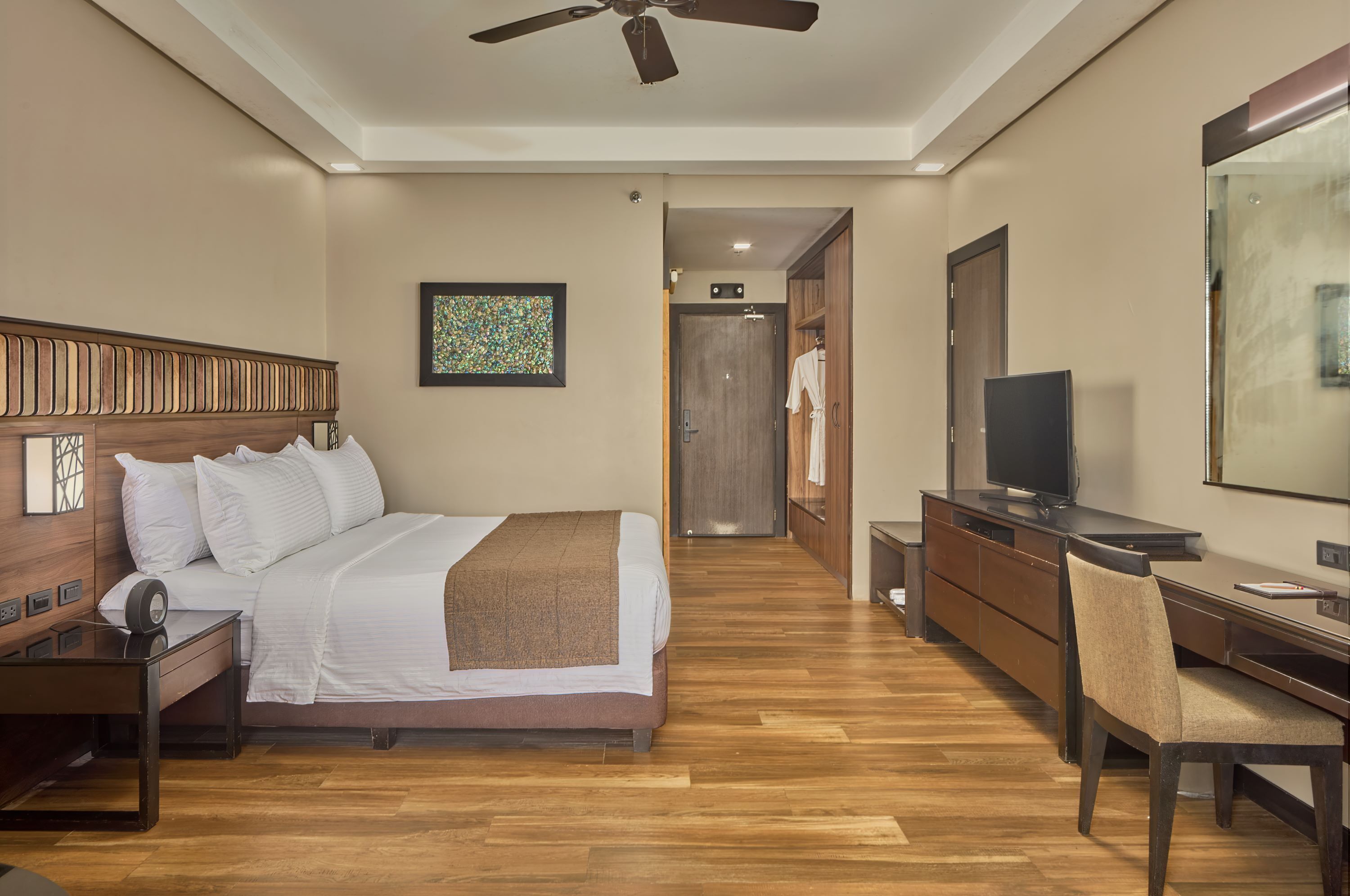 A hotel room with a bed, a desk, a chair, a television, and a ceiling fan.