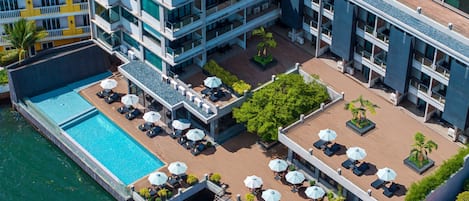 An aerial view of a hotel with a rooftop pool, outdoor seating areas, and multiple balconies.