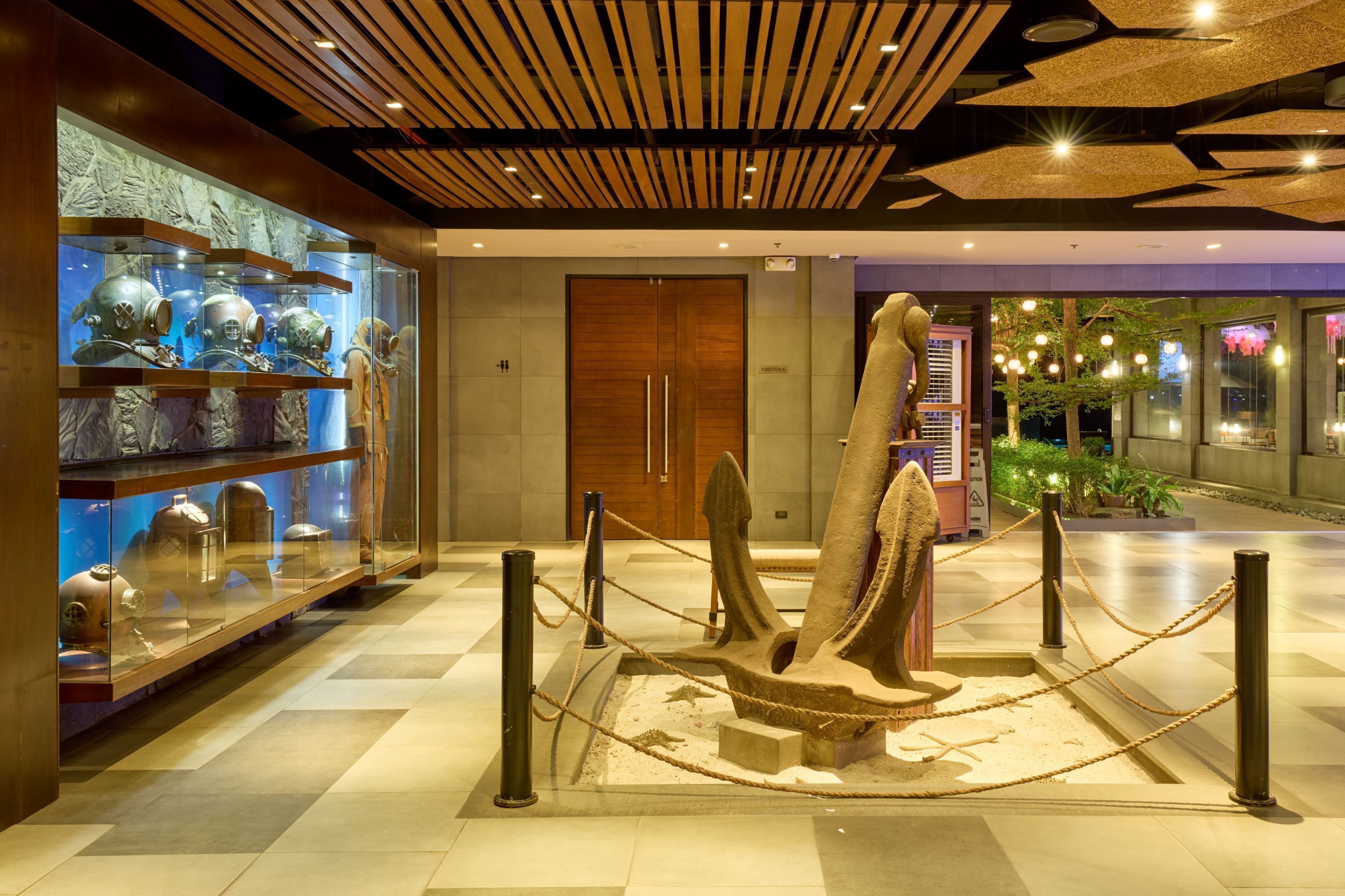 Eine Lobby mit einer großen Ankerskulptur, einer Vitrine mit Helmen und einer Holzbodenverkleidung.