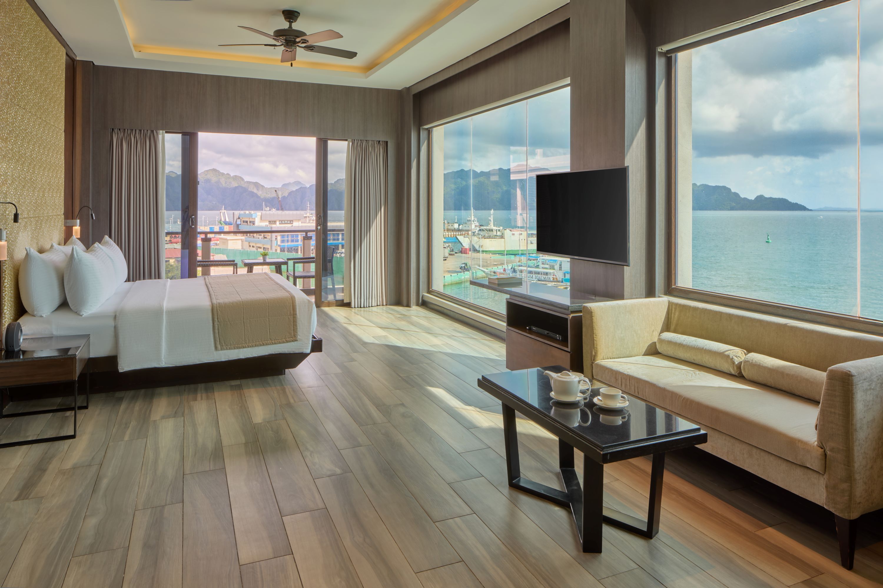 Habitación de hotel moderna con cama, sofá y balcón con vistas al mar y a las montañas.