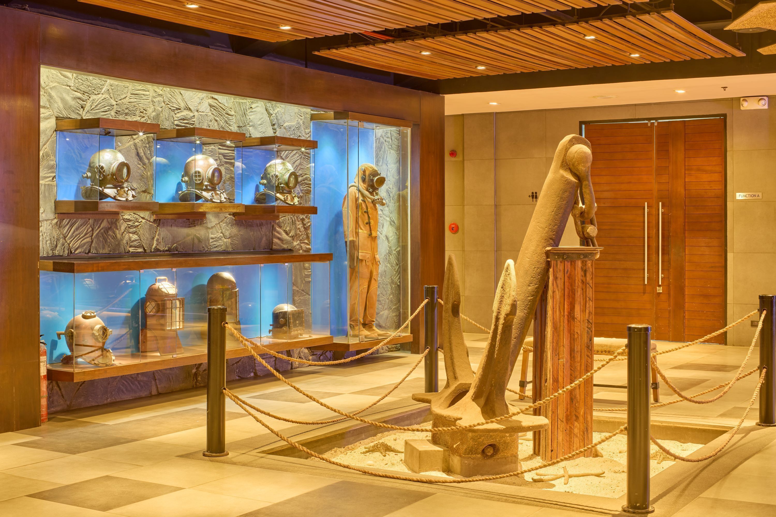 Une exposition de musée présentant des objets anciens, notamment une grande sculpture et des vitrines en verre.