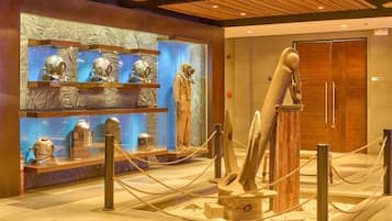 Une exposition de musée présentant des objets anciens, notamment une grande sculpture et des vitrines en verre.