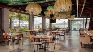 Un restaurante espacioso con numerosas mesas y sillas, amplias ventanas que ofrecen vista a un lago y montañas, y luces decorativas colgantes.