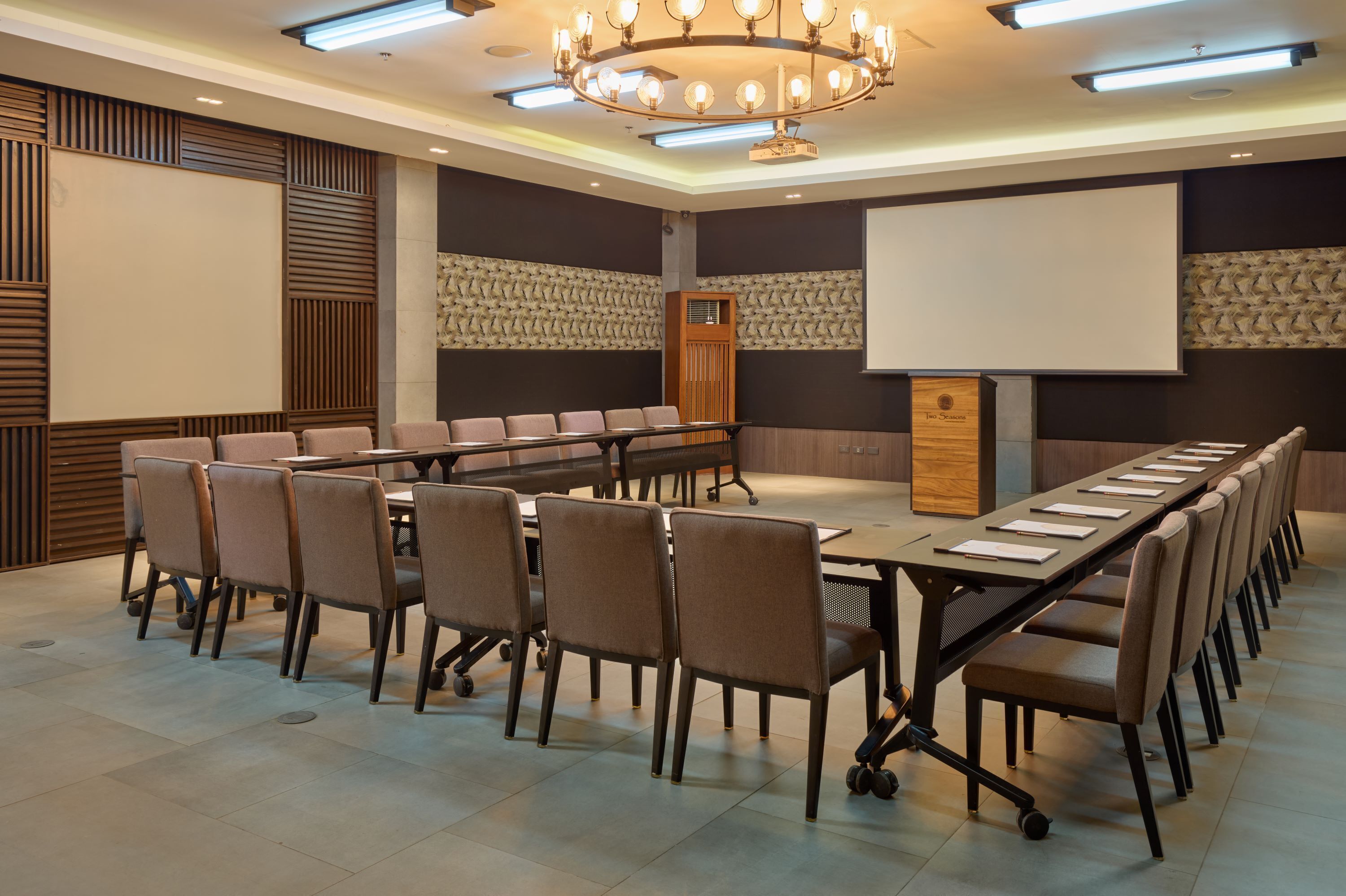Un salón de conferencias con una larga mesa, numerosas sillas, una pantalla de proyector y un atril de madera.