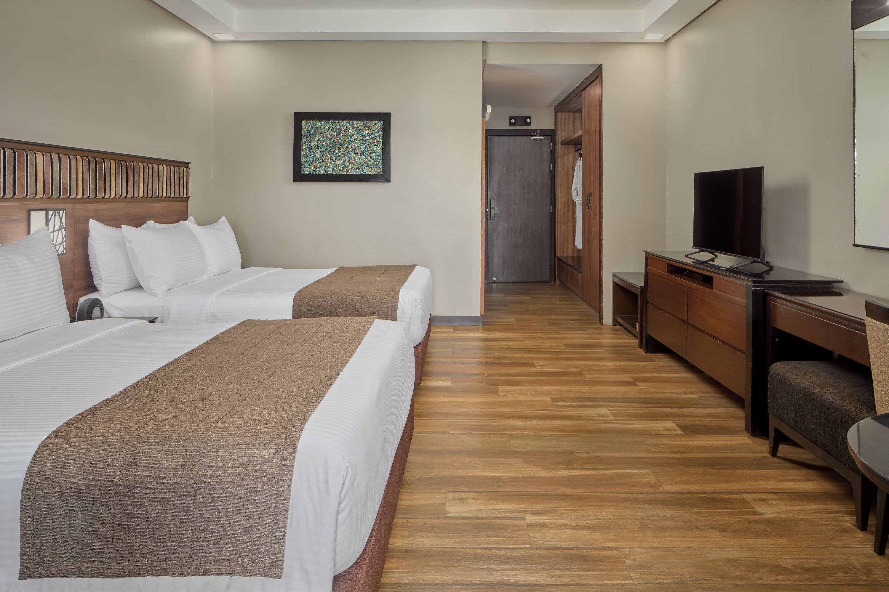 A hotel room with two beds, a desk, a television, and a wardrobe.