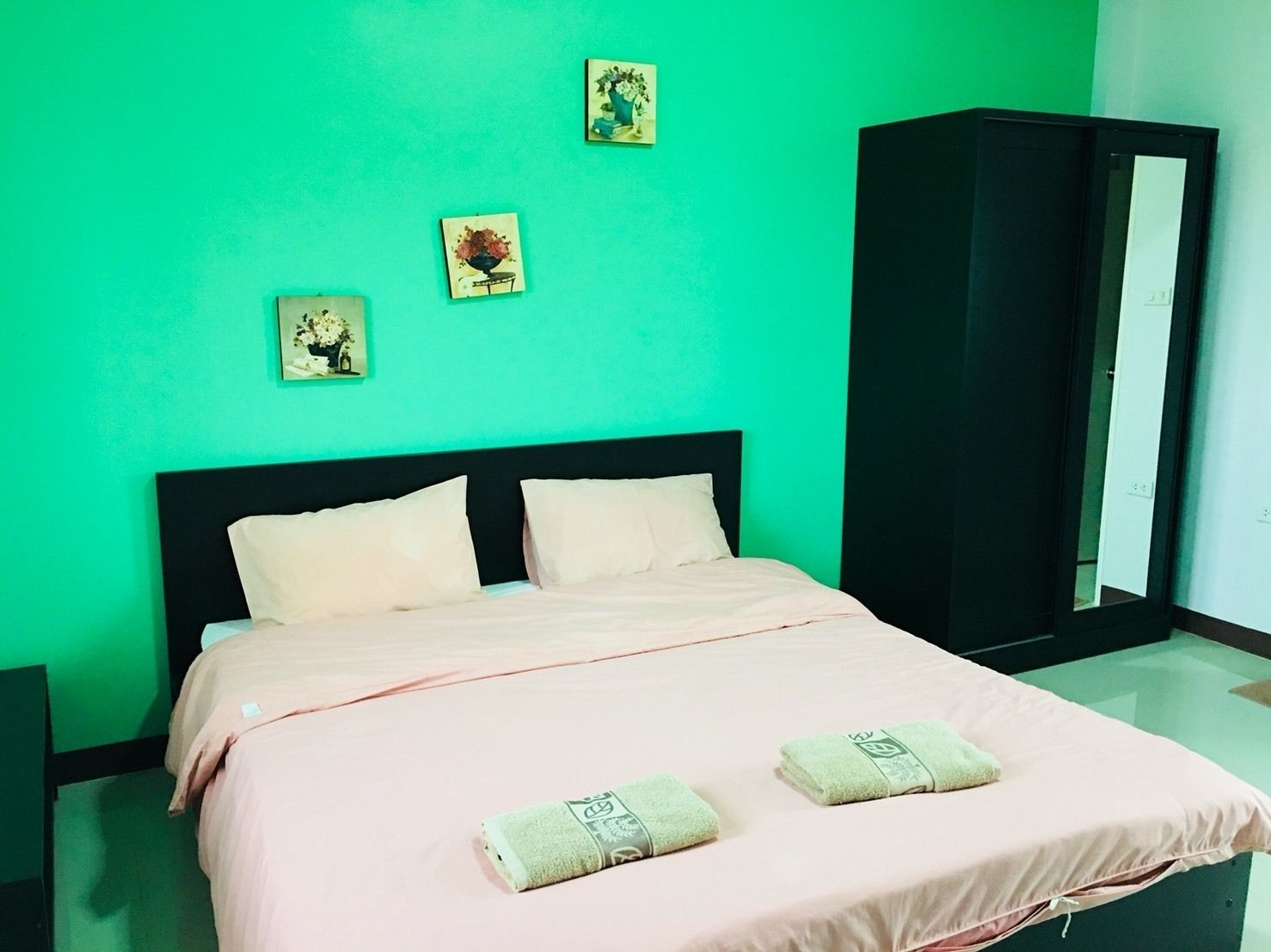 A bedroom with a bed, two pillows, a green wall, and three small framed pictures.