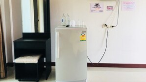 A room with a white refrigerator, a black cabinet, a television mounted on the wall, and a small table with bottles and a remote control. - The Rich Home (Nakhon Ratchasima)