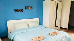 A bed with a blue bedspread and two towels, a white wardrobe, and two wall decorations. - The Rich Home (Nakhon Ratchasima)