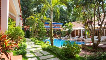 A pool area with a stone pathway, lounge chairs, and lush greenery.
