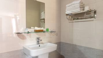 Une salle de bain avec un lavabo blanc, une étagère en verre où sont rangés les articles de toilette et un porte-serviettes avec des serviettes pliées.