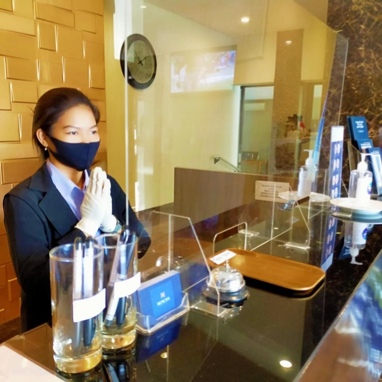 A hotel reception area with a glass counter, a clock, and a digital screen displaying information.