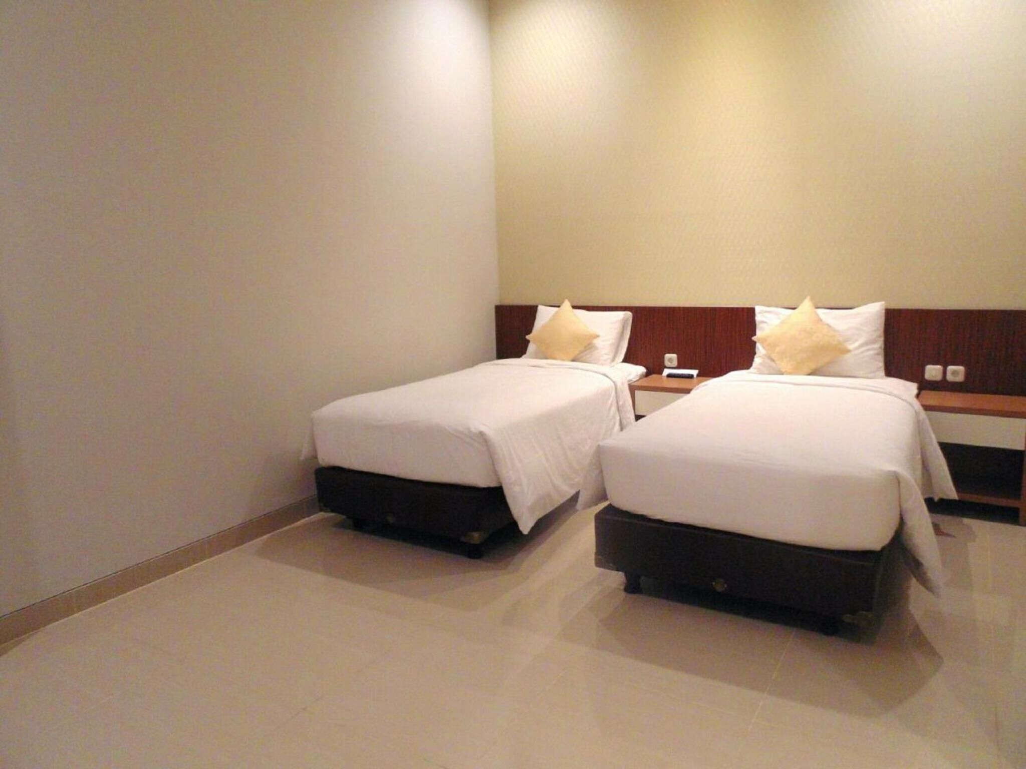 A hotel room with two single beds, each with a wooden headboard and white bedding.
