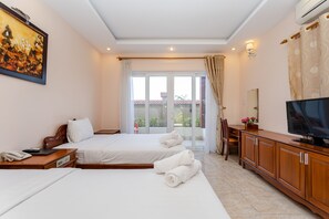 A hotel room with two beds, a TV, a desk, and a large window with curtains.