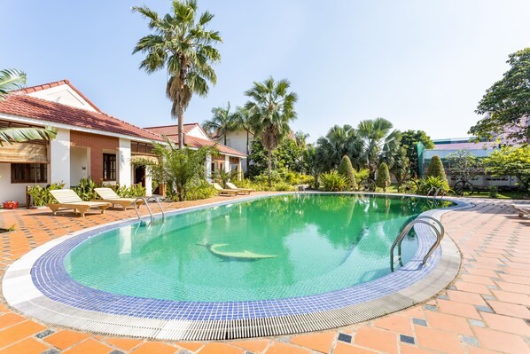 A swimming pool with a tiled edge, surrounded by lounge chairs and palm trees.