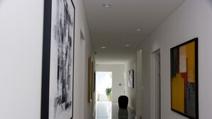 Un pasillo con obras de arte en las paredes, que conduce a una habitación luminosa con una planta.