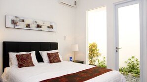 Una habitación de hotel con cama, mesita de noche, lámpara, ventana y puerta.