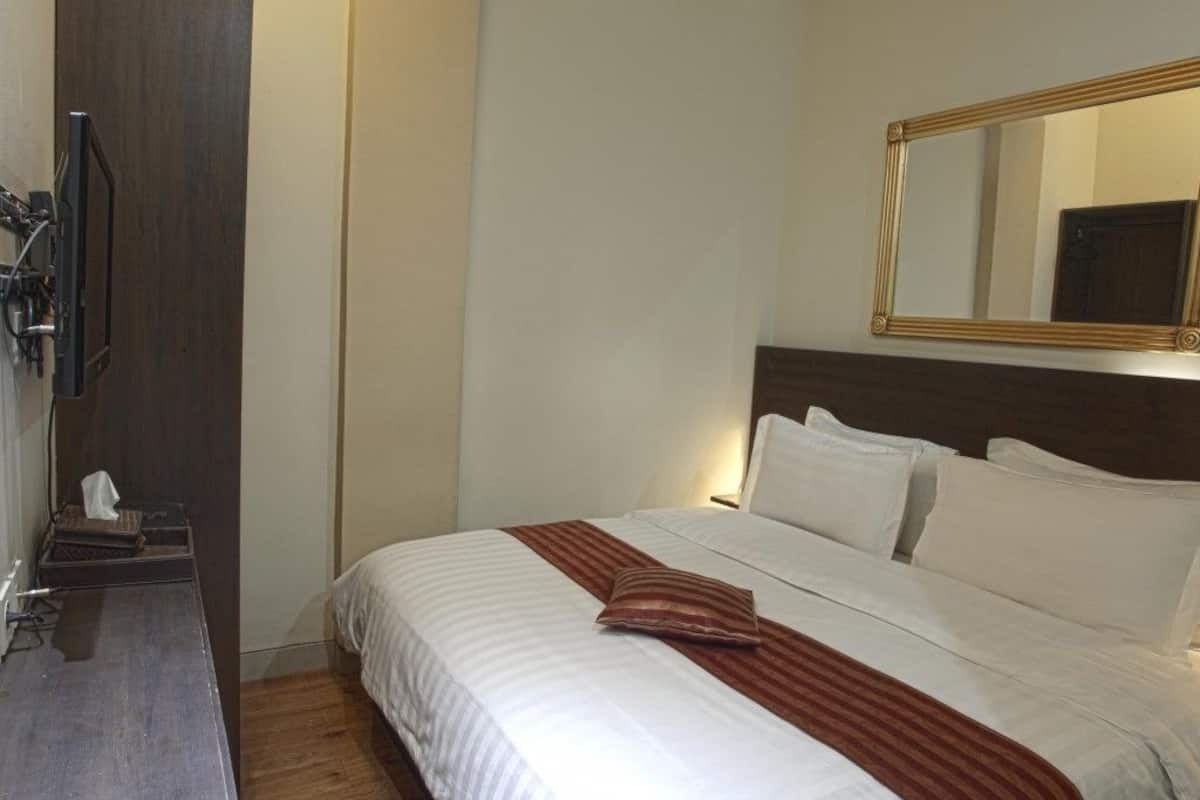 A hotel room with a bed, a wooden nightstand, a television, and a mirror on the wall.