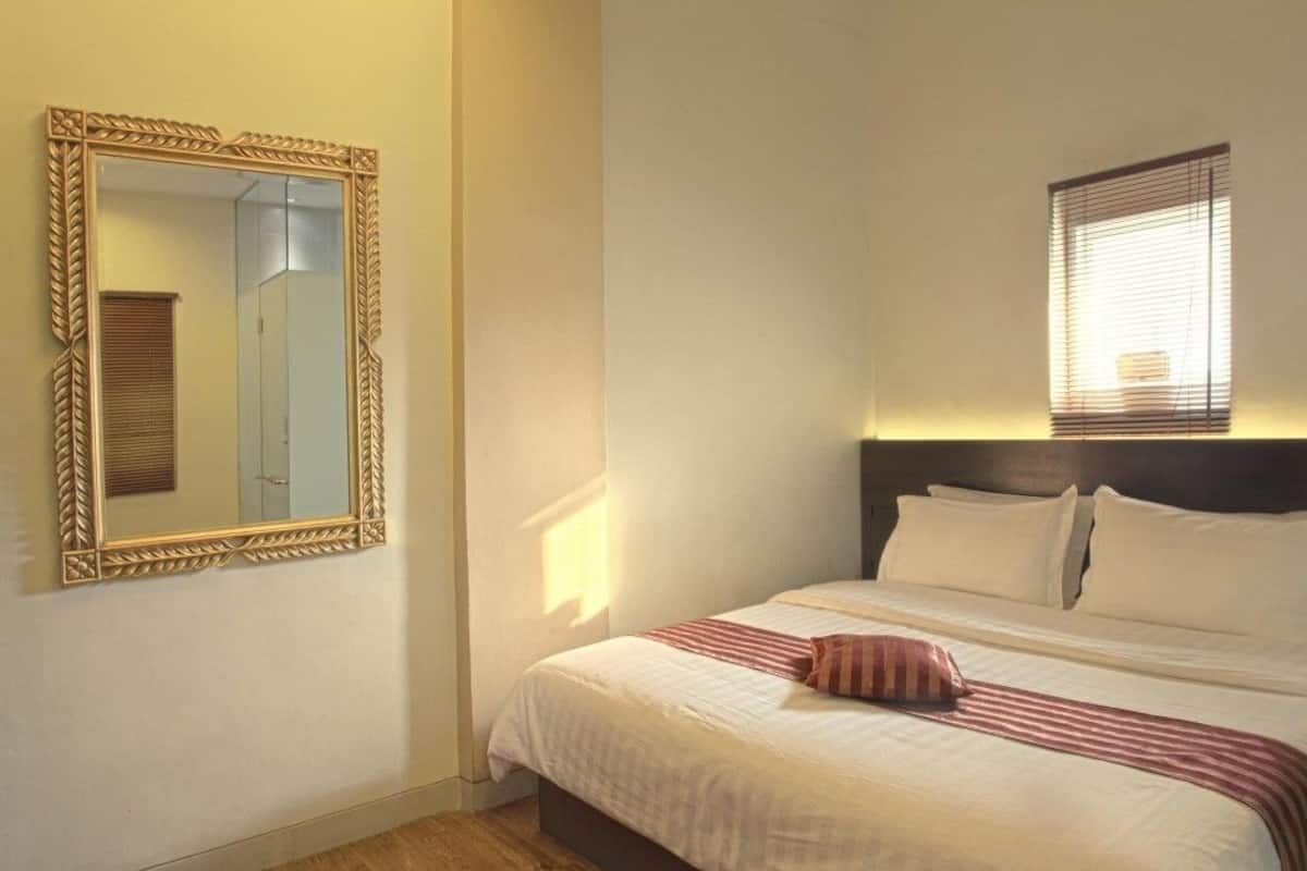 A hotel room with a large ornate mirror, a bed with white linens and a striped throw, and a window with blinds.