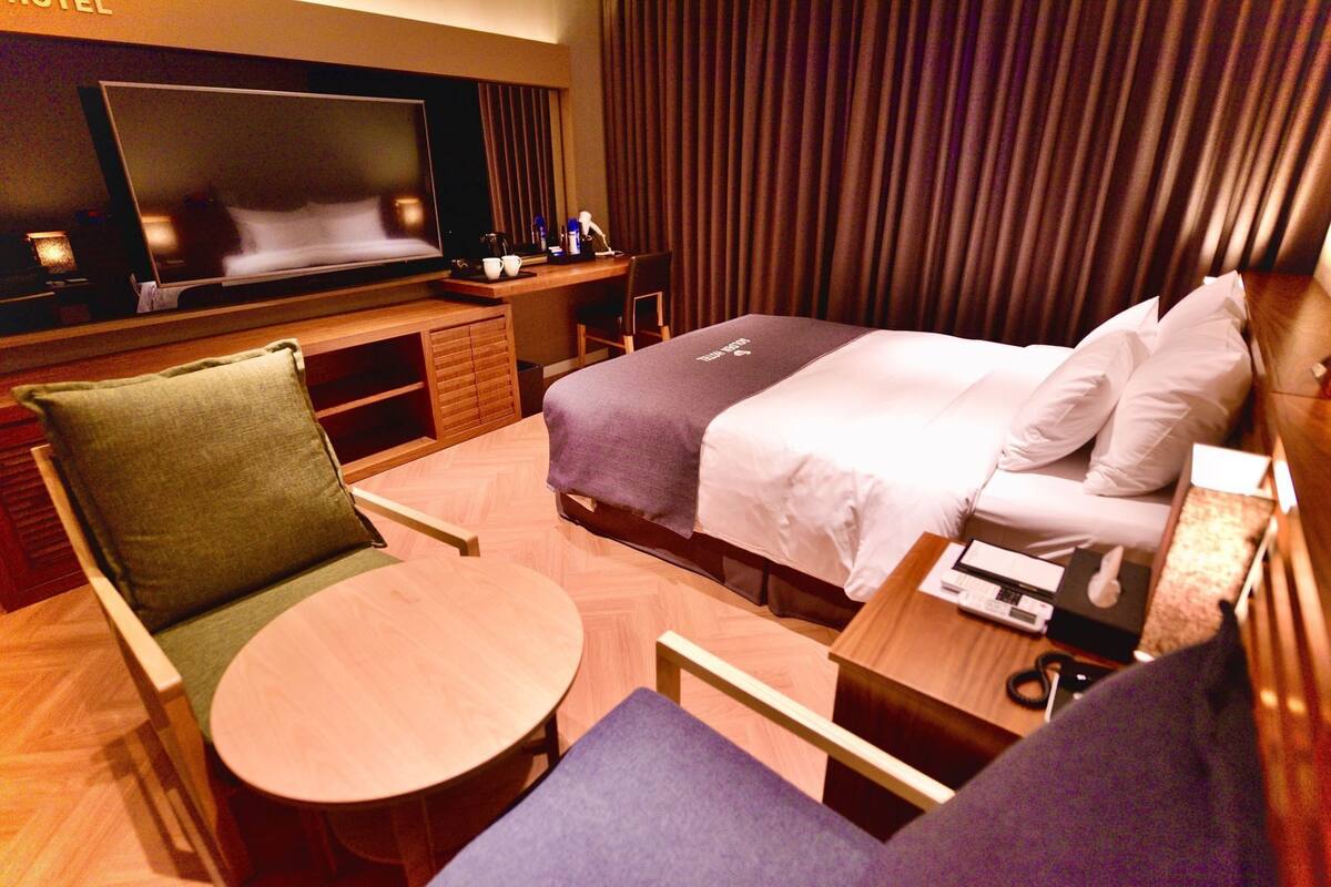 A hotel room with a bed, a TV, a desk, a chair, and a small table.