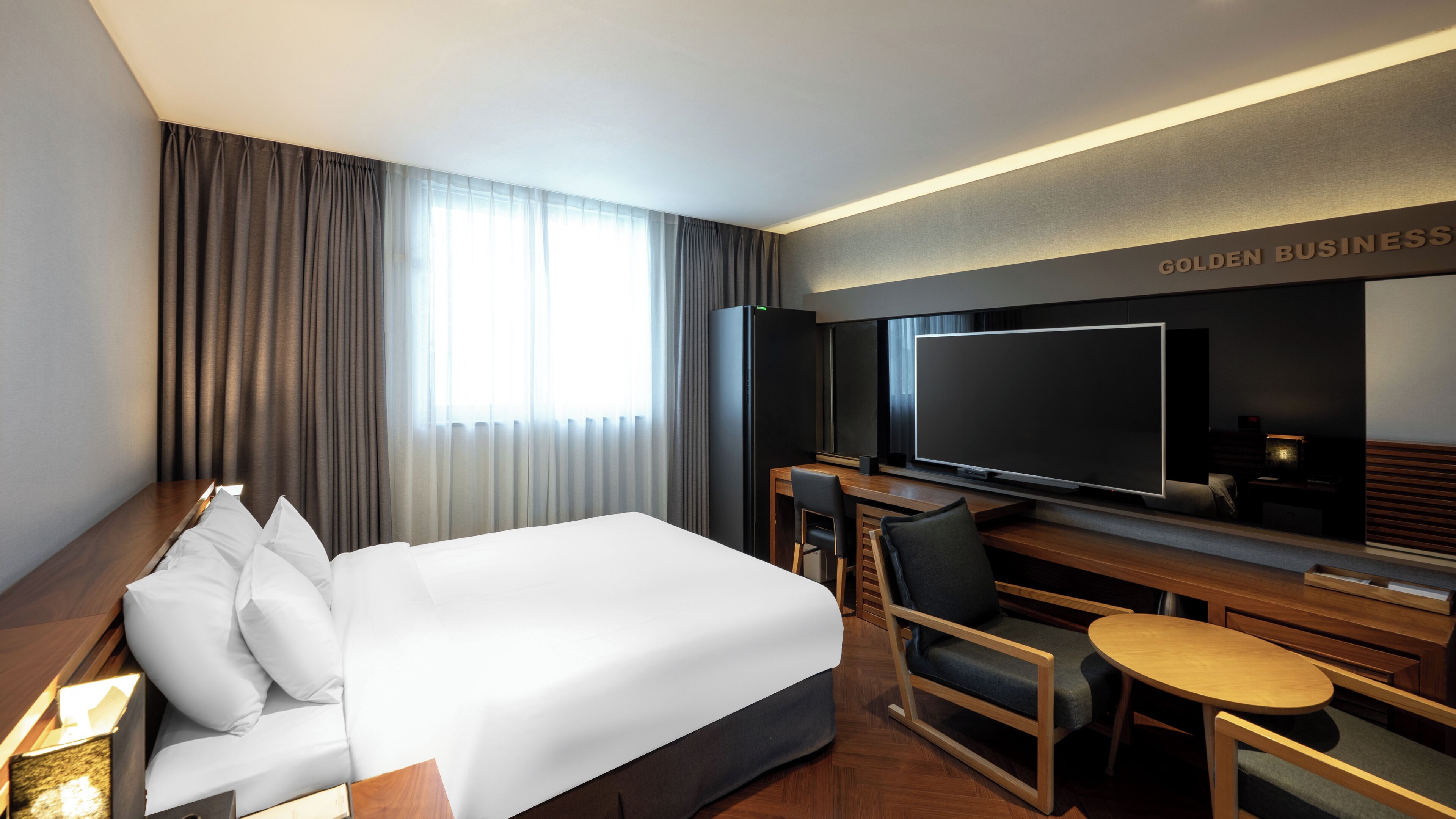 Una habitación de hotel con una cama grande, un escritorio con televisión de pantalla plana, una silla, una mesita redonda y un minibar.