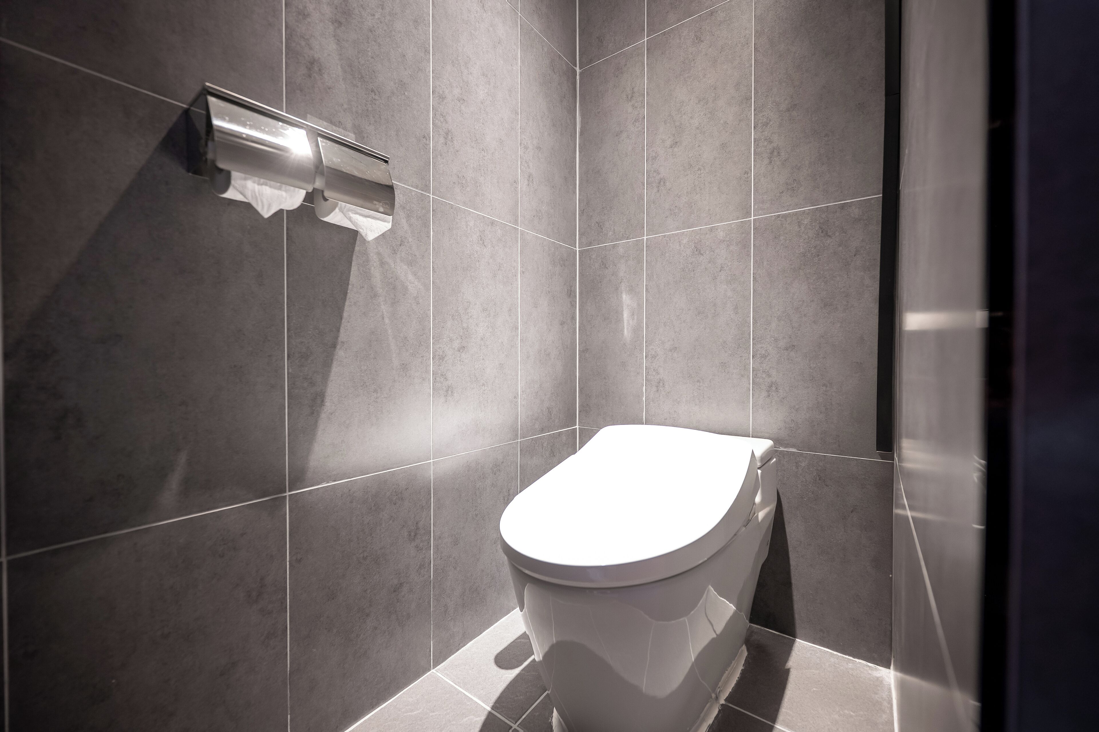 Un baño moderno con inodoro, dispensador de toallas y paredes de azulejos.