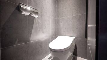 Un baño moderno con inodoro, dispensador de toallas y paredes de azulejos.
