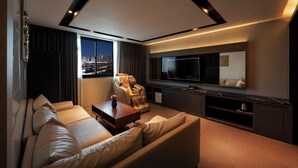 Una sala moderna con sofá de cuero, butaca de masaje, televisor y vista a la ciudad.
