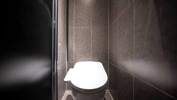 Un baño moderno con inodoro blanco, paredes de azulejos oscuros y cabina de ducha de cristal.