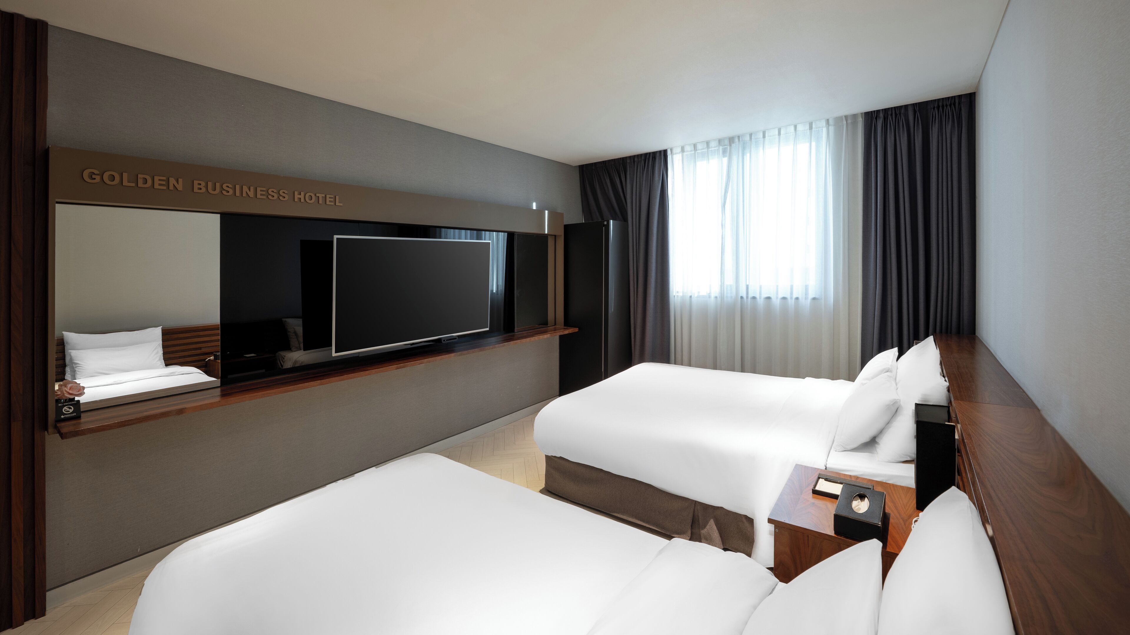 A hotel room with two beds, a flat-screen TV, a wooden desk, and a large window with curtains.