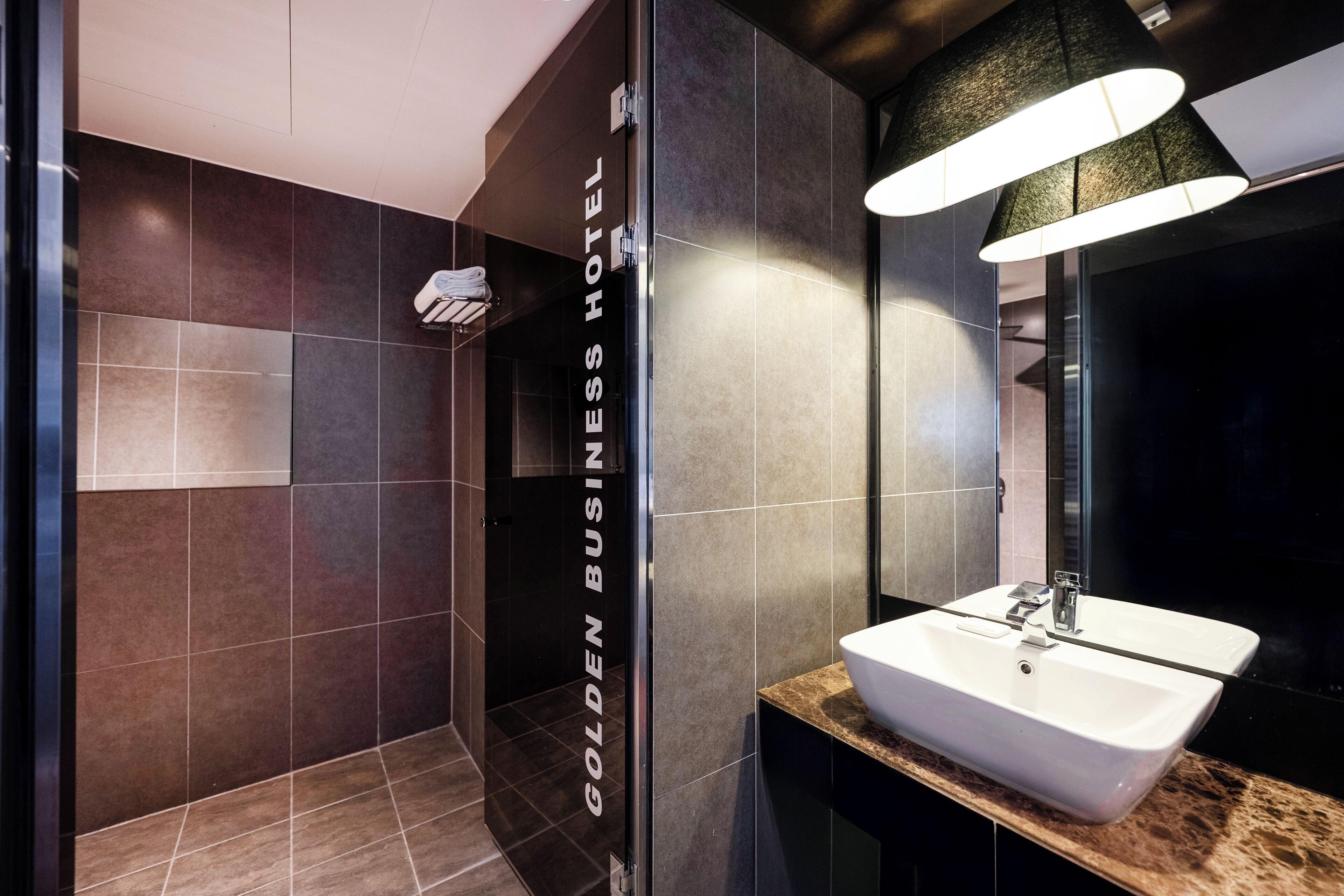 A modern bathroom with a large mirror, a white sink, and a shower area.