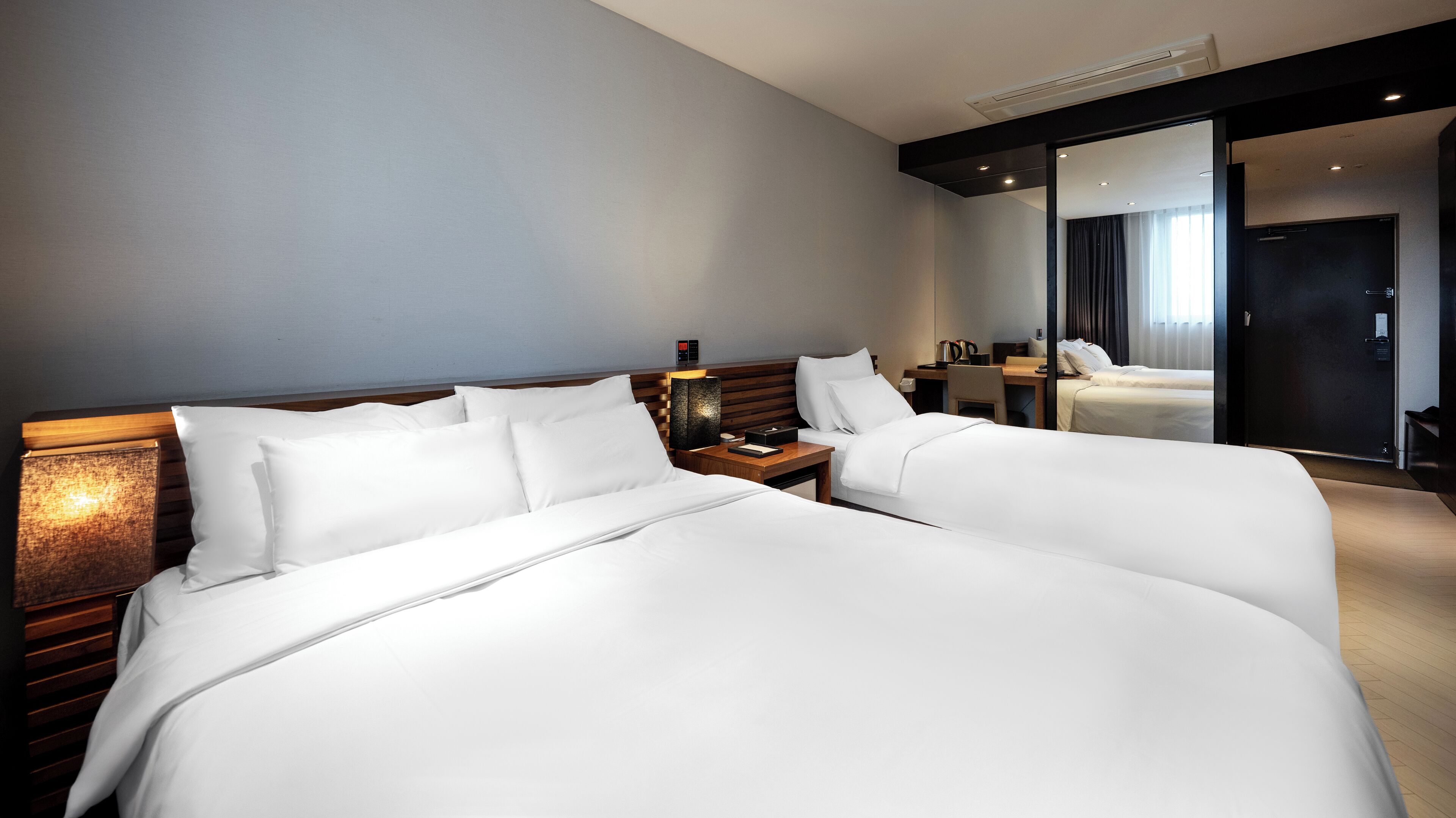 Hotelkamer met twee grote bedden, een bureau, een stoel, een nachtkastje en een spiegel.