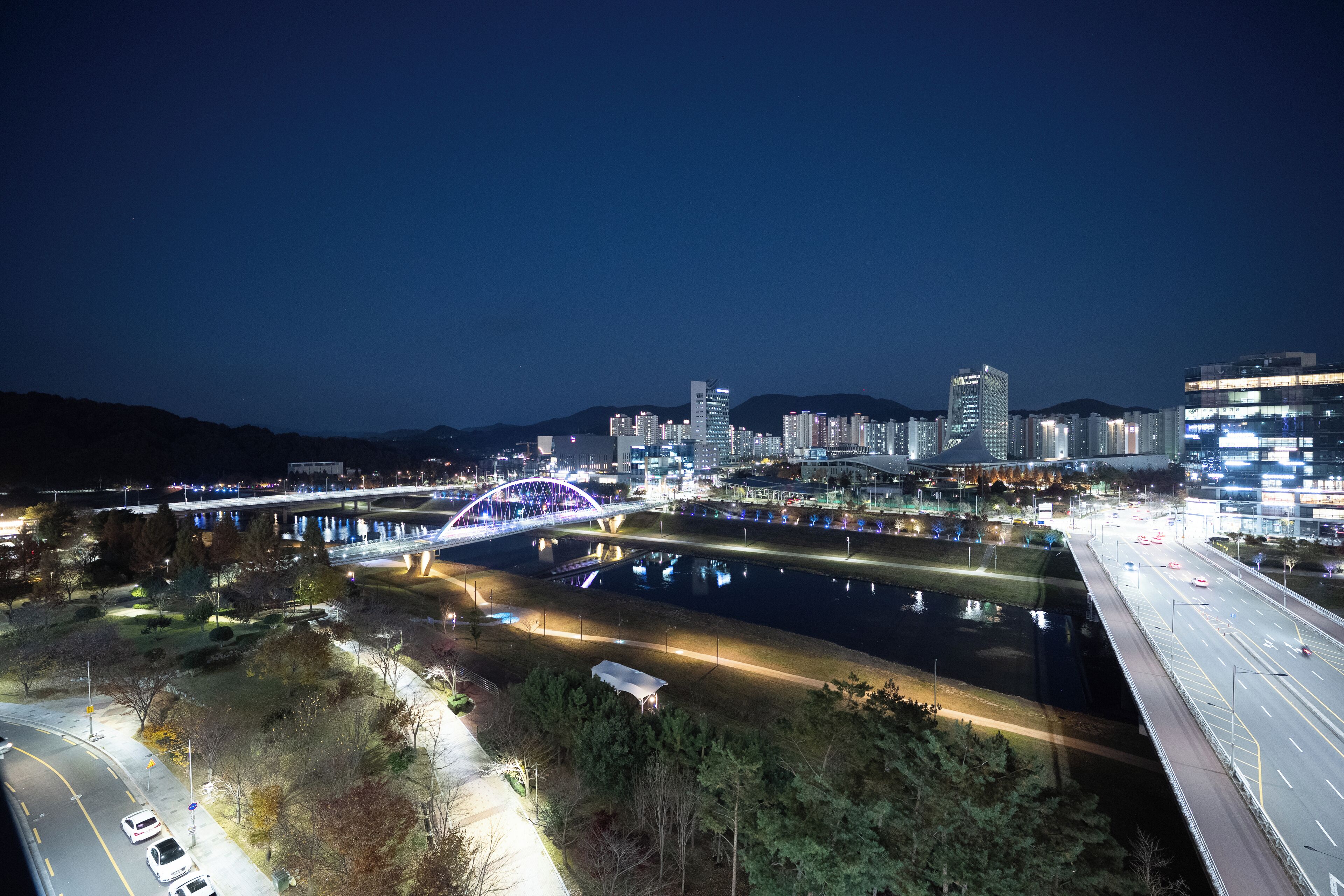 Un paisaje urbano nocturno con un puente iluminado destacado, un río y edificios altos.
