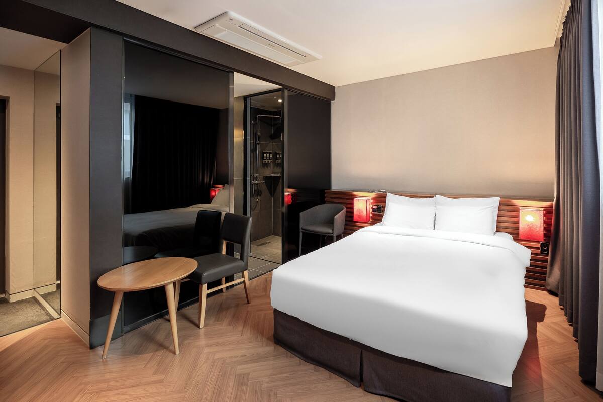 A hotel room with a large bed, a small table, a chair, and a mirror.