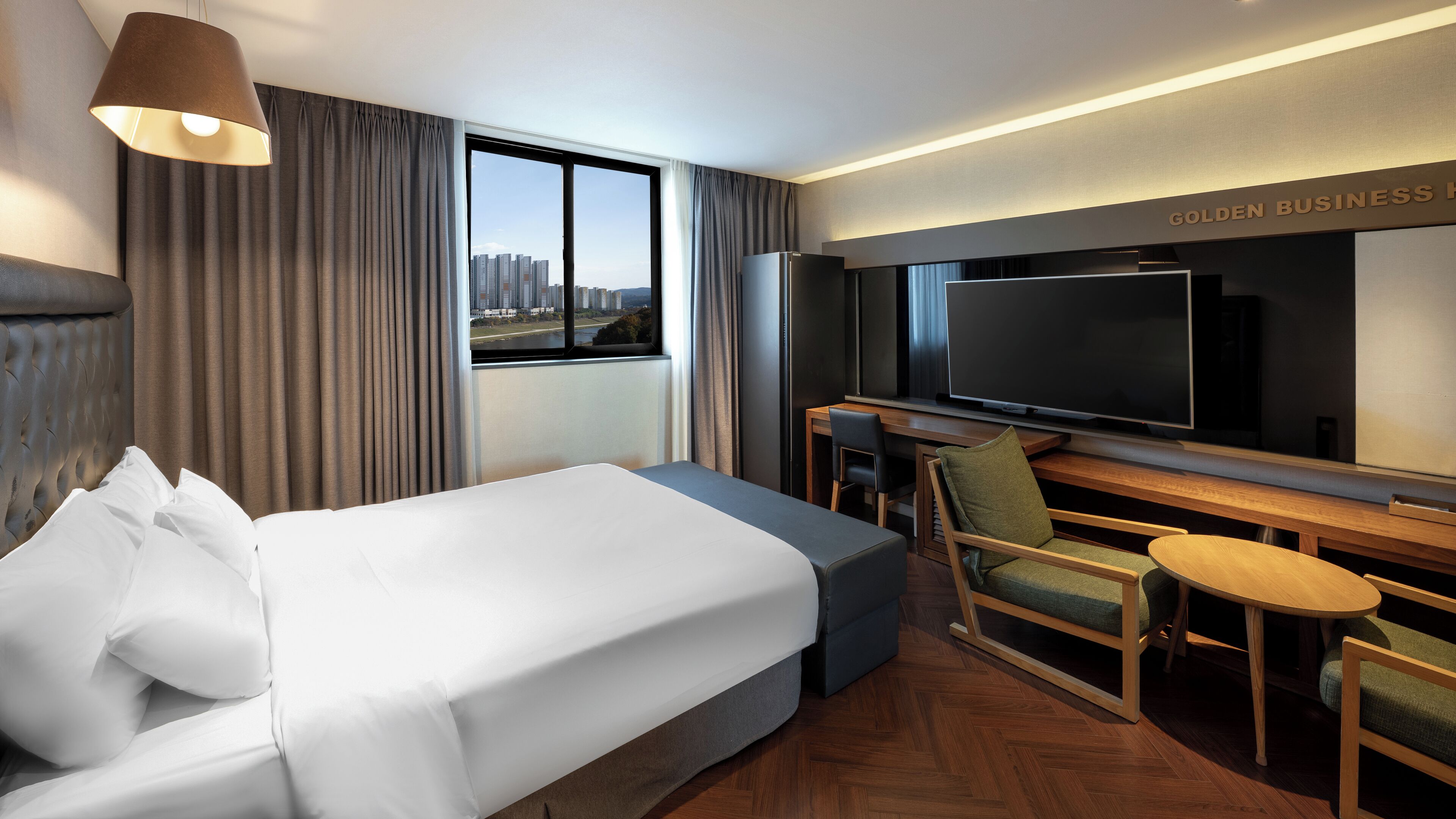 A hotel room with a bed, a desk, a chair, a television, and a view of the cityscape.