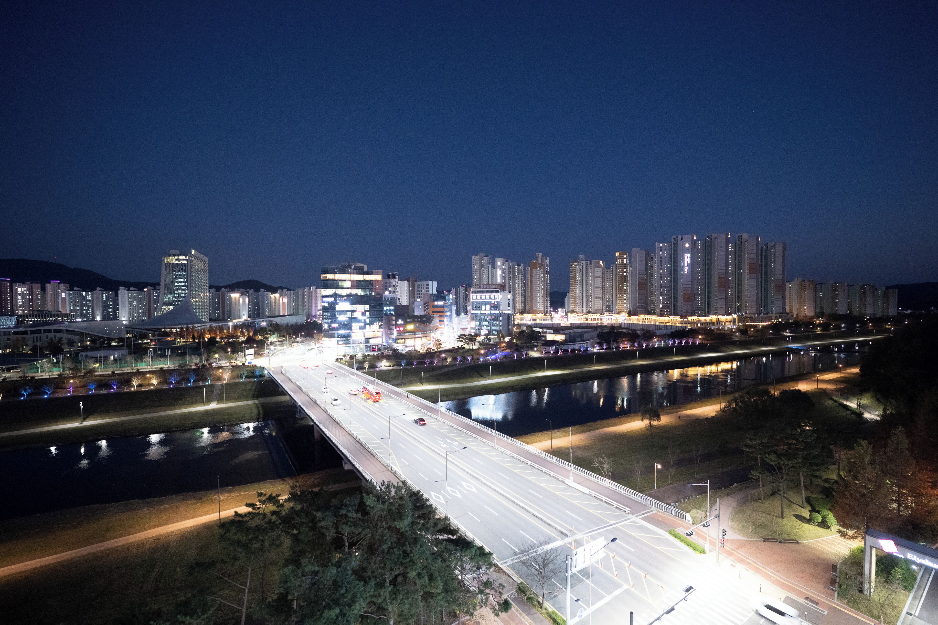 A nighttime cityscape with a river, a bridge, and high-rise buildings.