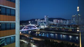 Paisatge urbà nocturn amb un pont brillant sobre un riu, edificis moderns i una vista clara de l'horitzó de la ciutat.