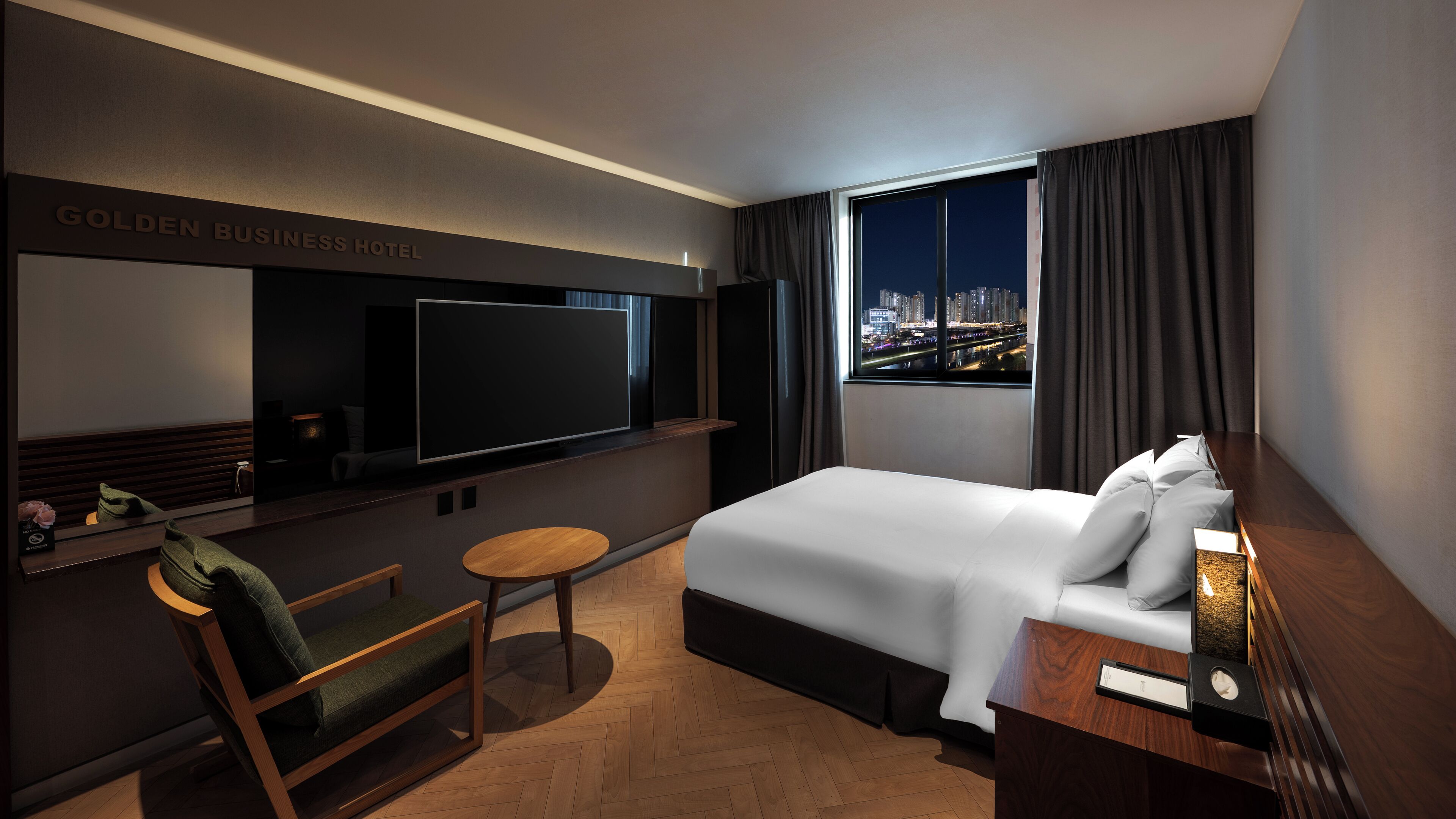 Een hotelkamer met een bed, een televisie, een bureau, een stoel en uitzicht op de stad.