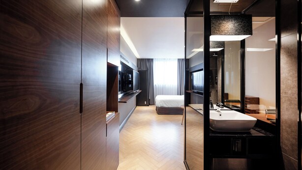 Una habitación de hotel moderna con un armario de madera, un espejo grande, una cama y un baño con lavamanos y espejo.