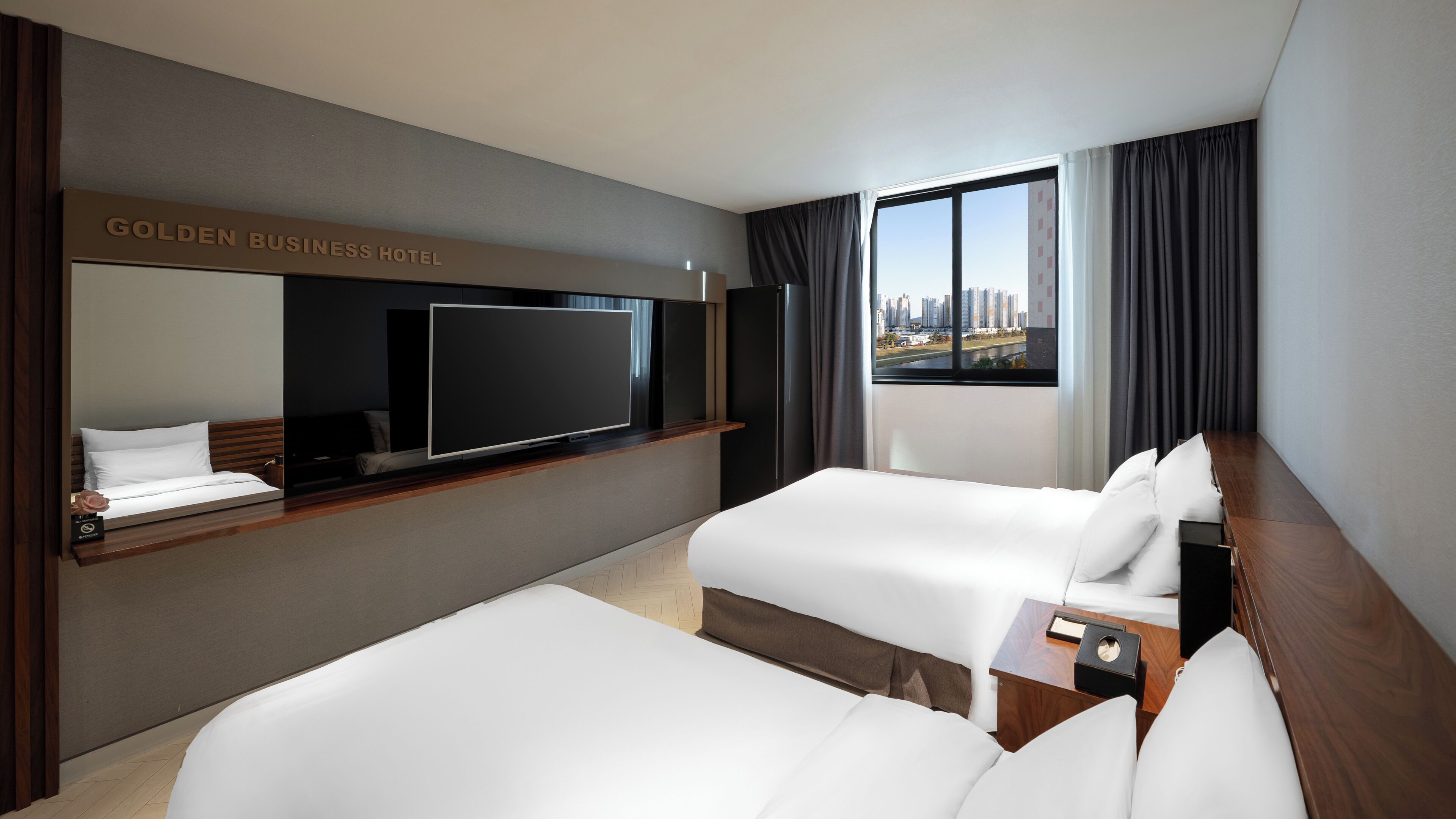 A hotel room with two beds, a flat-screen TV, a wooden desk, and a city view.